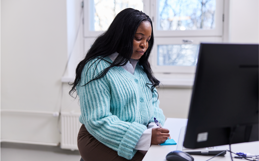 Henkilö kirjoittaa muistiinpanoja toimistossa tietokoneen äärellä.