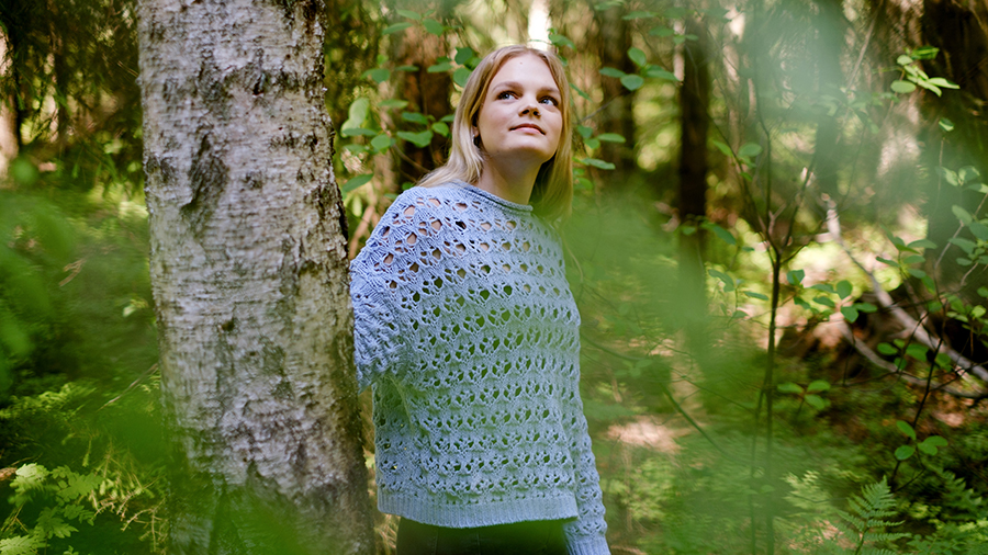 Nuori henkilö seisoo metsässä ja katsoo ylöspäin.