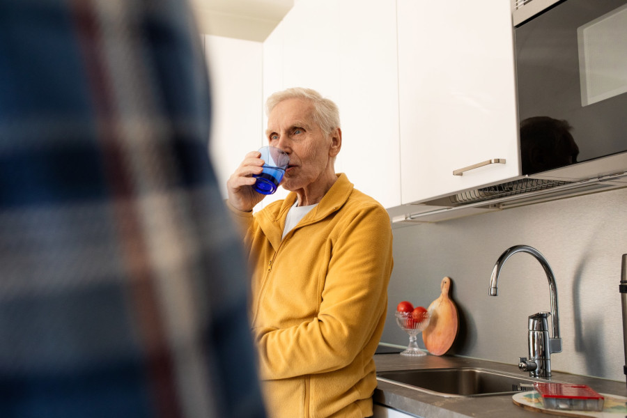 A pensioner drinks water in the kitchen.