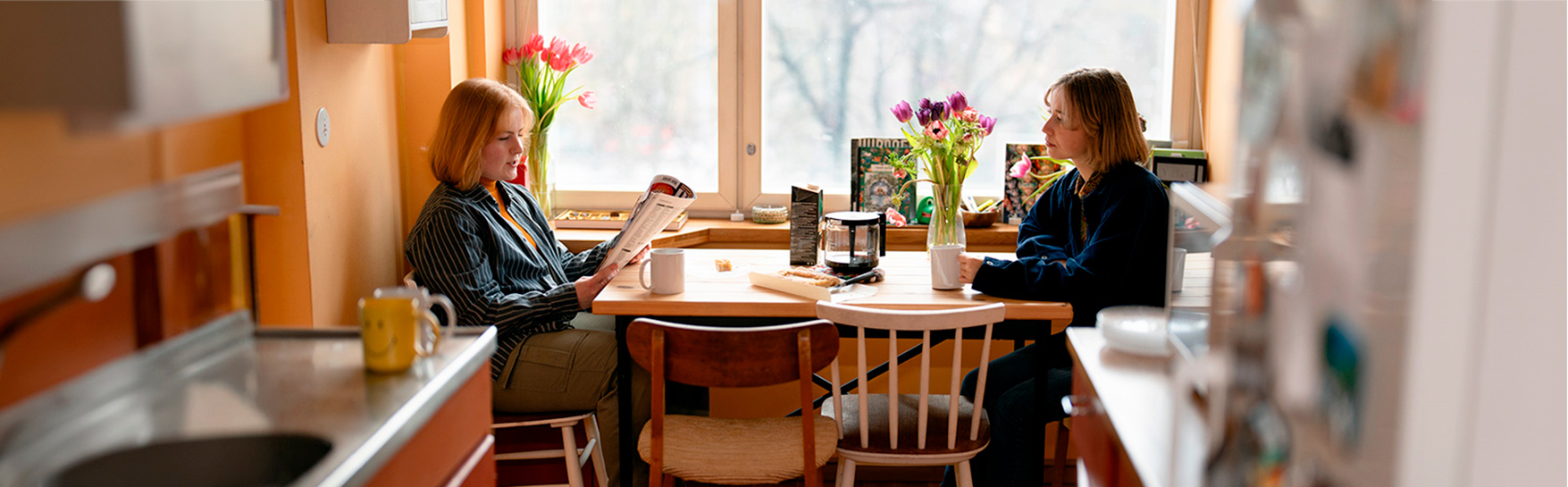 Two young people are sitting at a table in a kitchen.